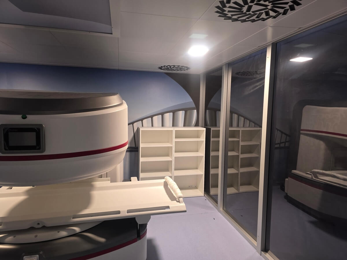 MRI suite with superconducting scanner showing ceiling-mounted quench pipe routing and emergency ventilation infrastructure